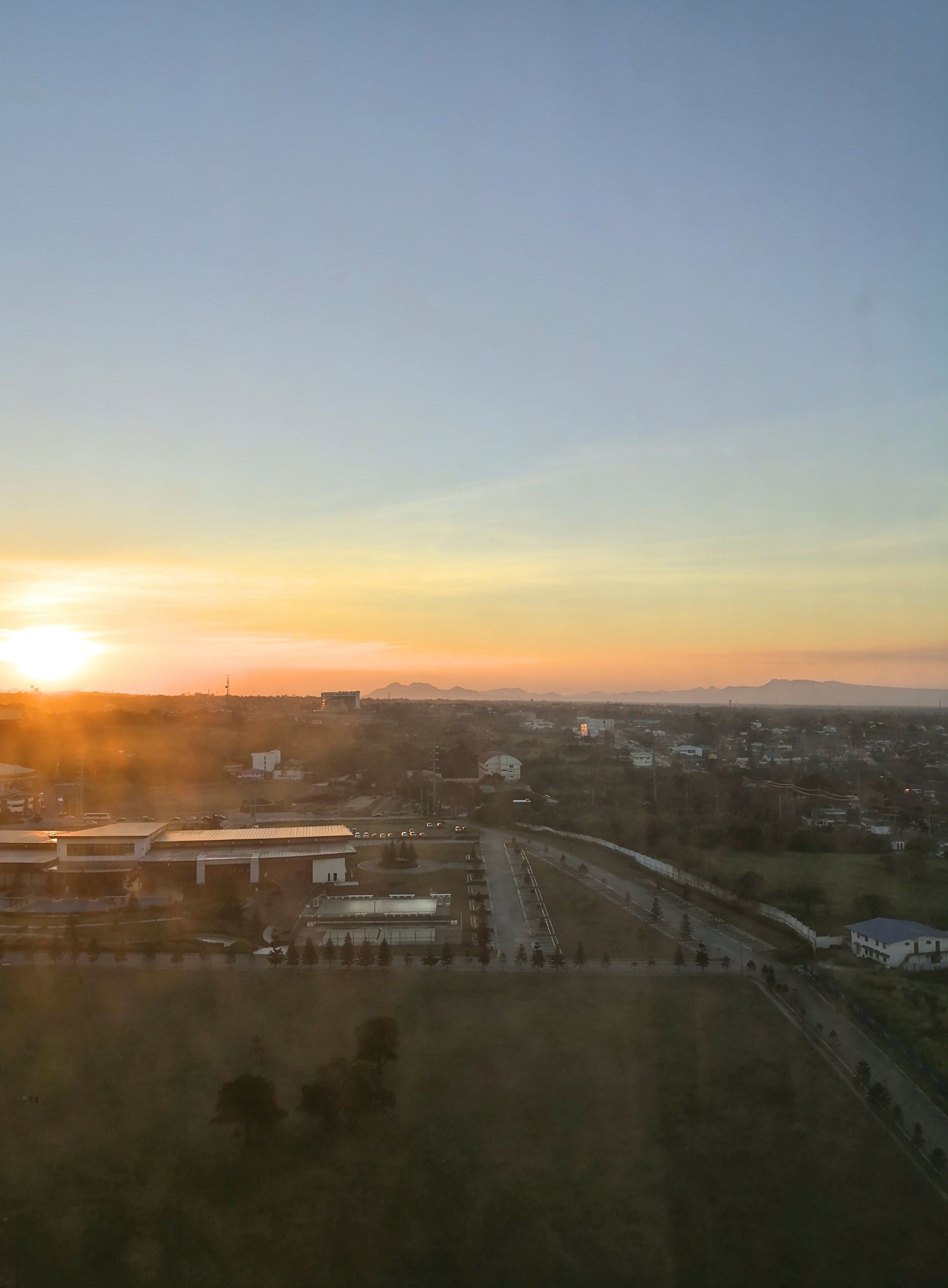 An aerial view of a cityscape during sunset with buildings, roads, and a clear sky.