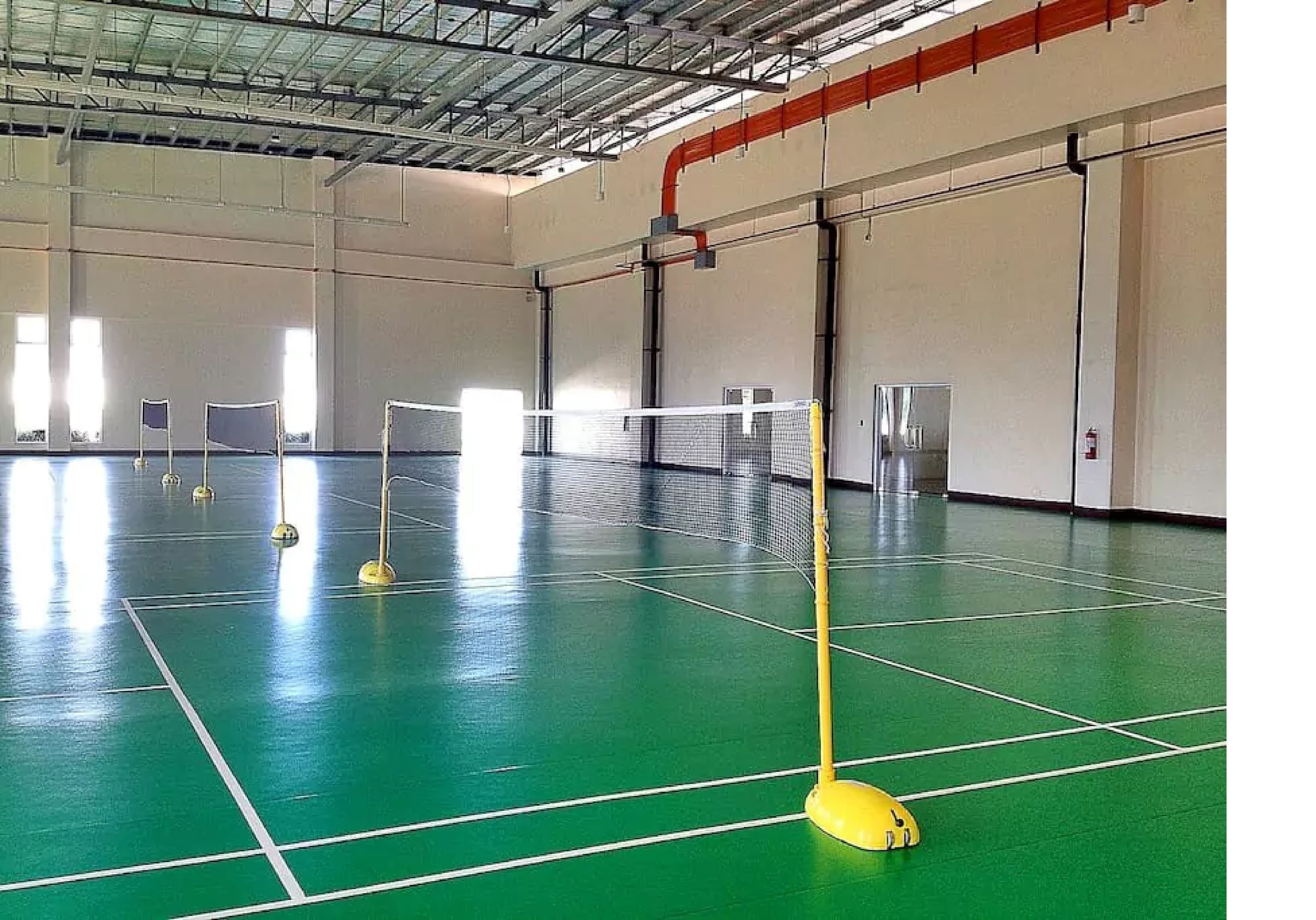 An indoor sports facility with a green floor, white lines marking a court, and a yellow net.