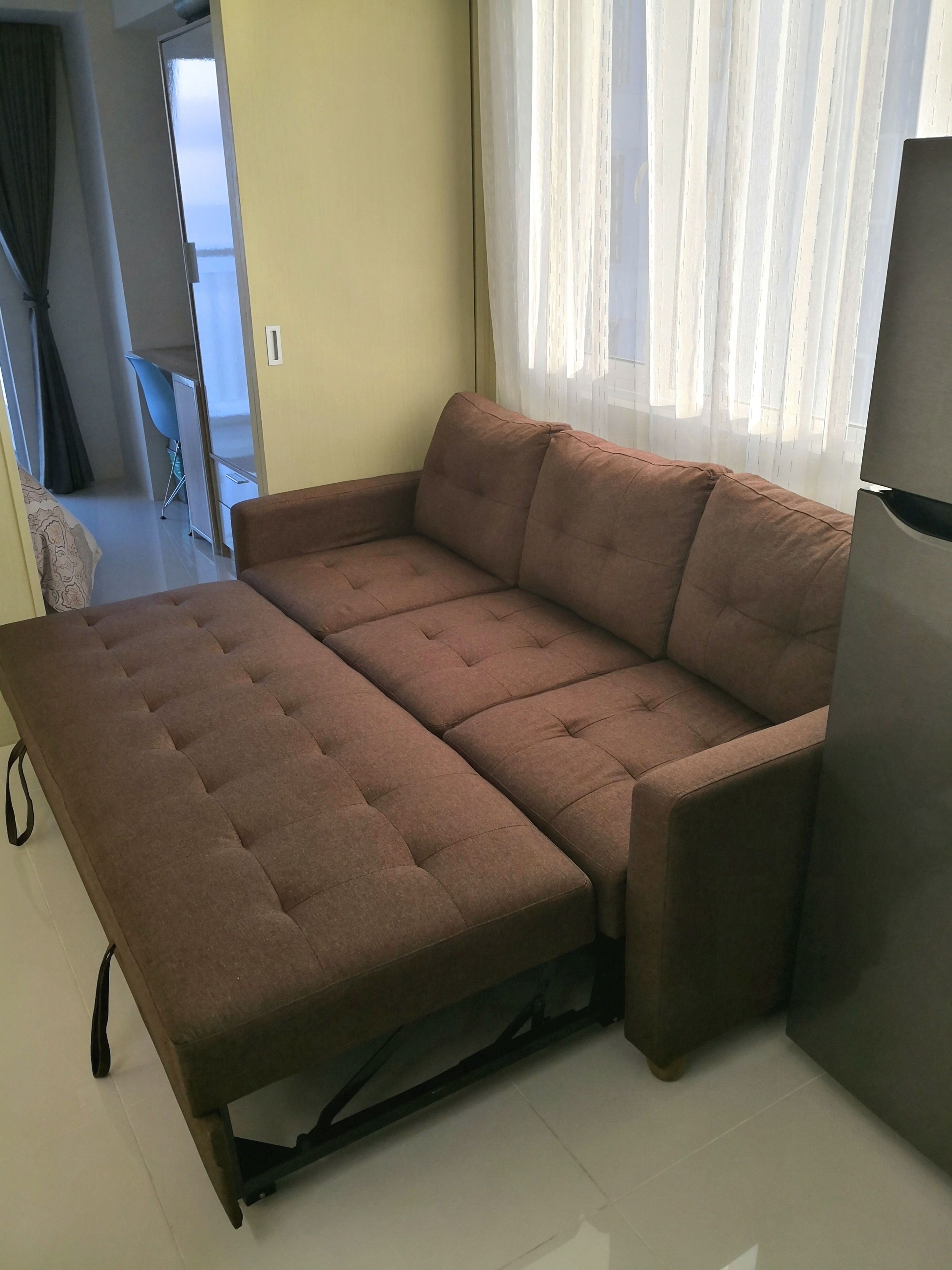 Un canapé marron avec une fonction convertible se trouve dans une pièce dotée d’une fenêtre et d’une porte donnant sur une autre pièce.