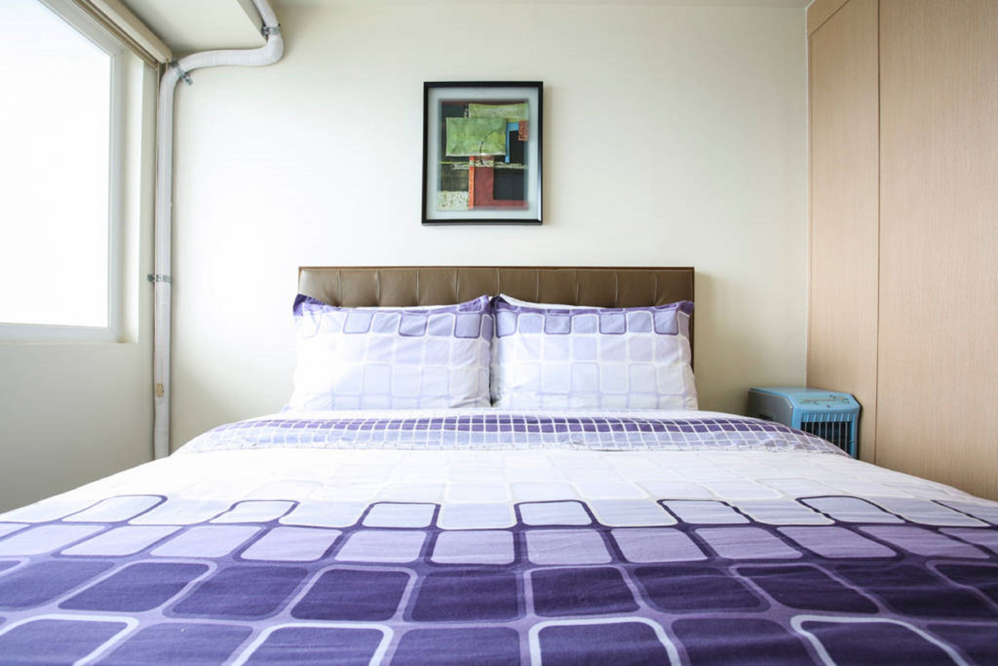 A neatly made bed with a patterned bedspread, a framed picture on the wall, and a window on the left side.