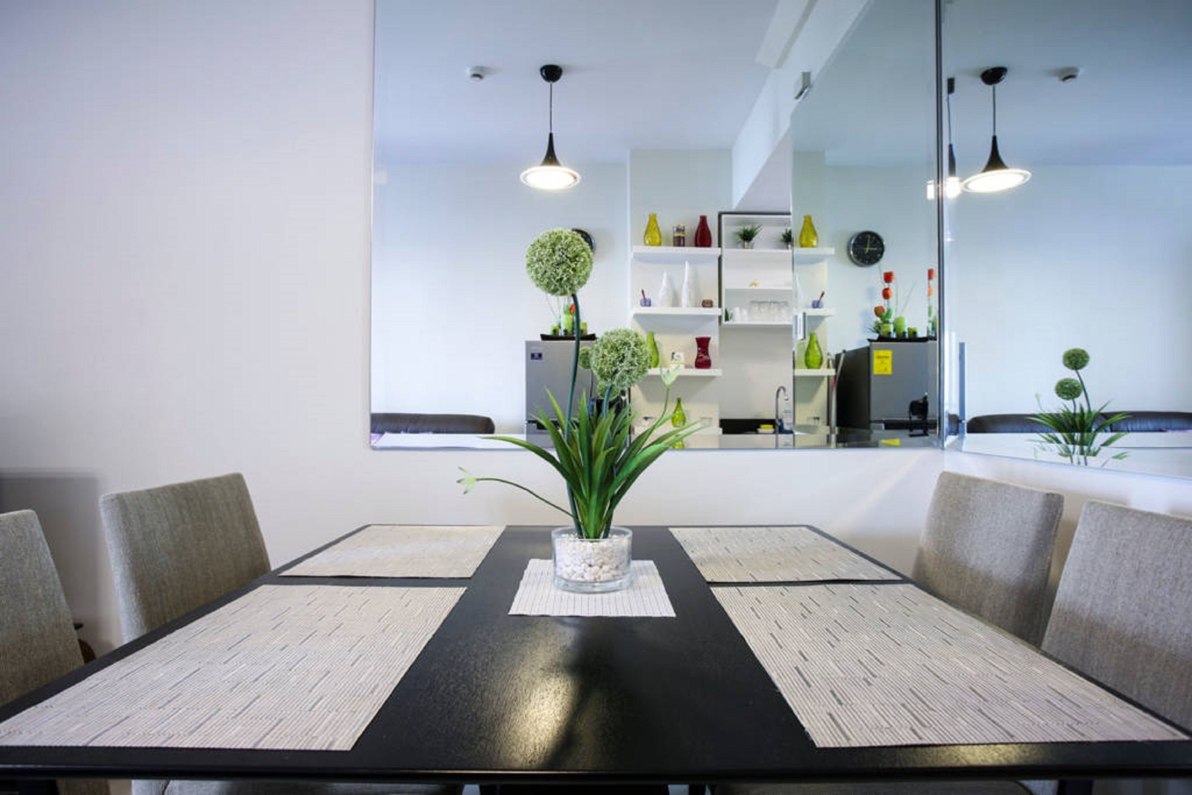 A conference room with a black table, white placemats, and grey chairs. There is a potted plant on the table.