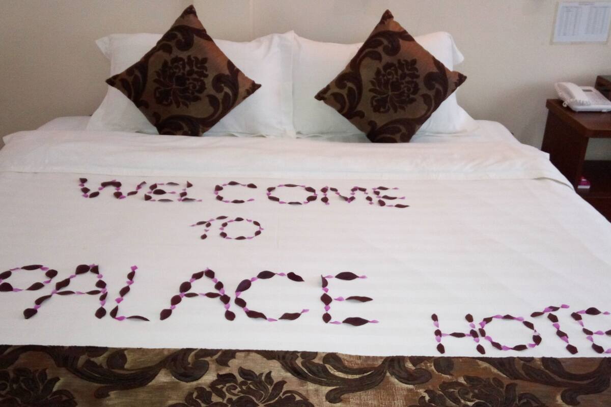 A bed with a welcome mat to the Palace Hotel.