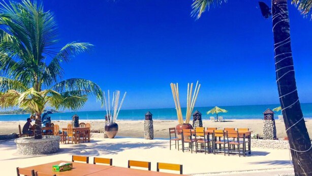 A beachside restaurant with outdoor seating, palm trees, and a view of the ocean. - Kyauk Phyu Palace Resort Hotel (Kyaukpyu)