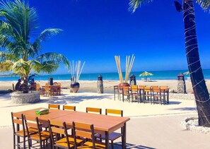 A beachside restaurant with outdoor seating, palm trees, and a view of the ocean. - Kyauk Phyu Palace Resort Hotel (Kyaukpyu)
