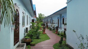 A corridor with a wooden pathway flanked by buildings with blue roofs and white walls. - Kyauk Phyu Palace Resort Hotel (Kyaukpyu)