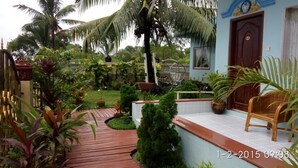 A tropical garden with a wooden deck, potted plants, and a wicker chair. - Kyauk Phyu Palace Resort Hotel (Kyaukpyu)