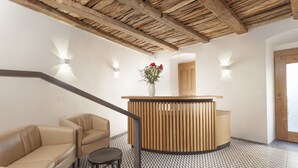 A reception area with a wooden reception desk, a beige sofa, a small round table, and a patterned floor. - Hotel At the White Lily (Prague)