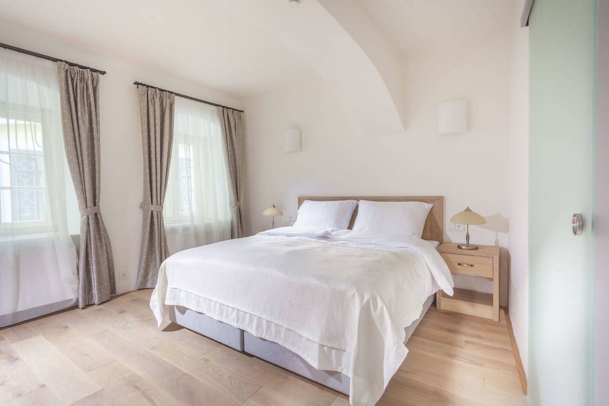 Un dormitorio con cama, mesitas de noche y ventana con cortinas.