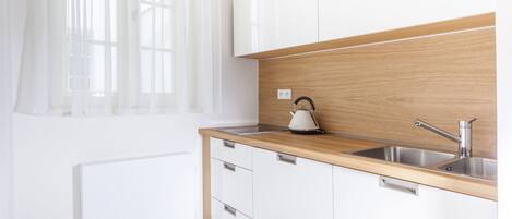A modern kitchen with white cabinets, a wooden countertop, and a stainless steel sink.