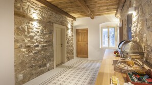 A rustic interior with stone walls, wooden beams, a buffet with pastries, and a view through a door. - Hotel At the White Lily (Prague)