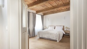 A bedroom with a wooden ceiling, a bed with white linens, a nightstand with a lamp, and patterned curtains. - Hotel At the White Lily (Prague)