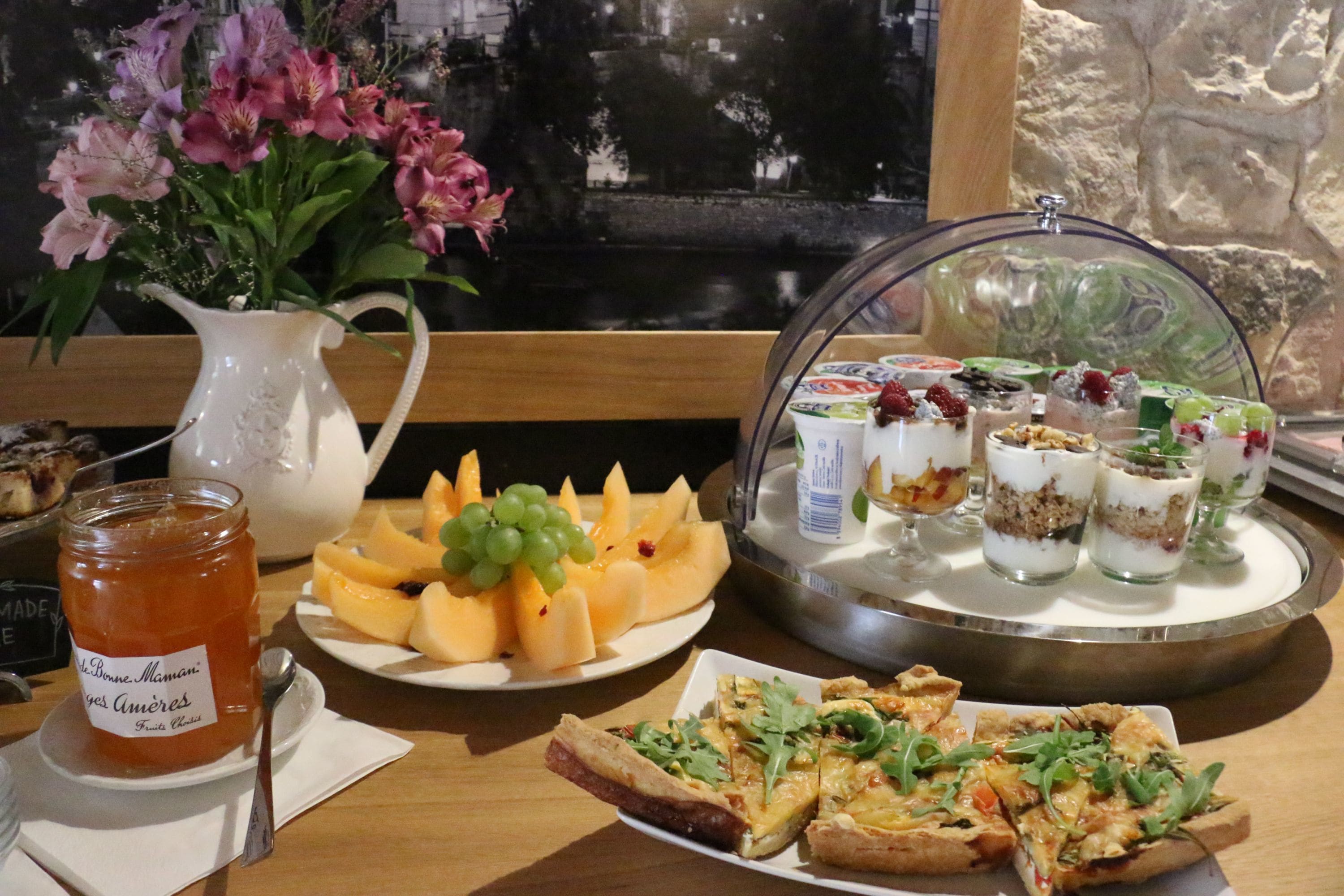 A table with a variety of food items including a pitcher of jam, a plate of fruit, and a tray of desserts.