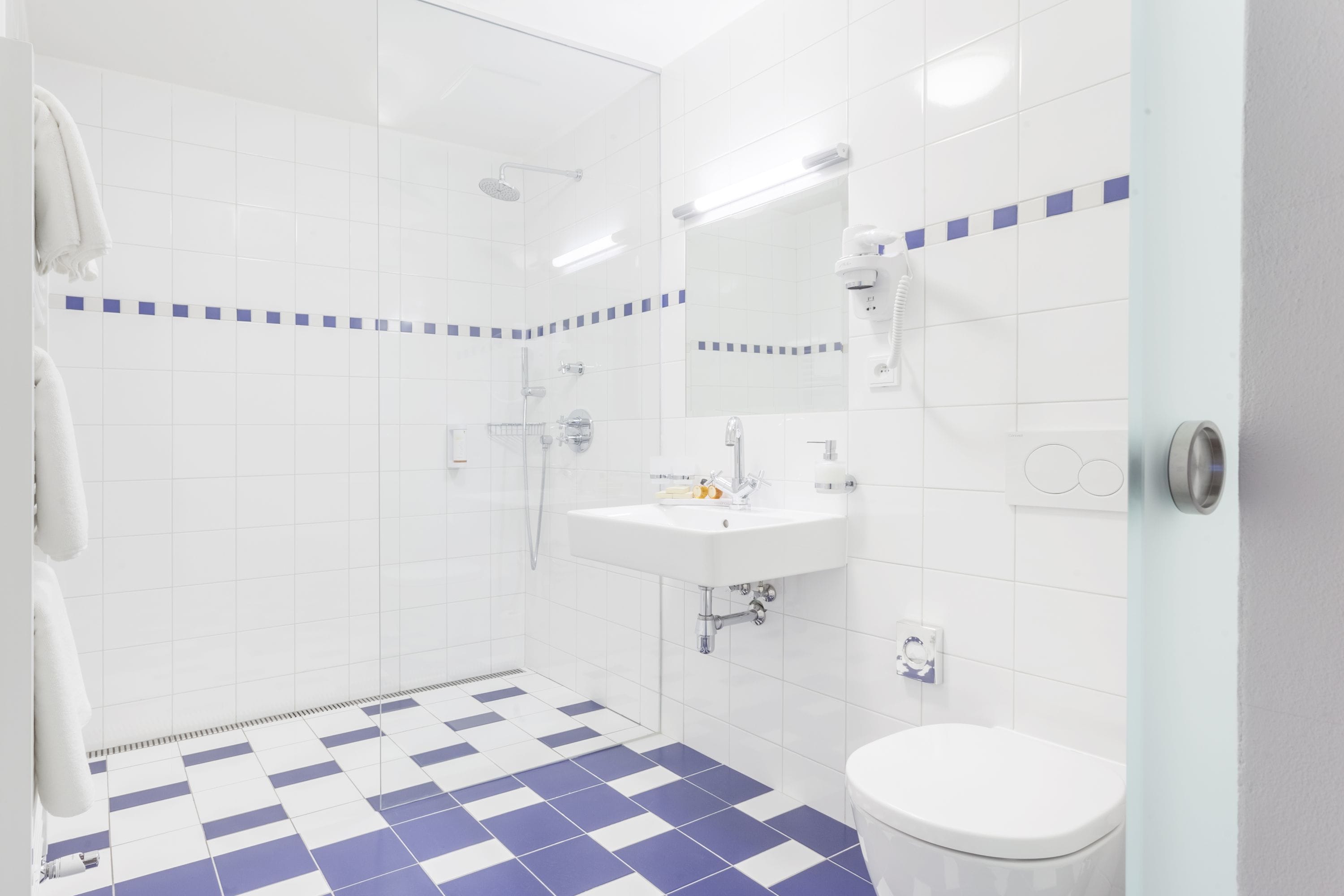 A modern bathroom with a checkered floor, a white sink, a toilet, and a glass shower enclosure.
