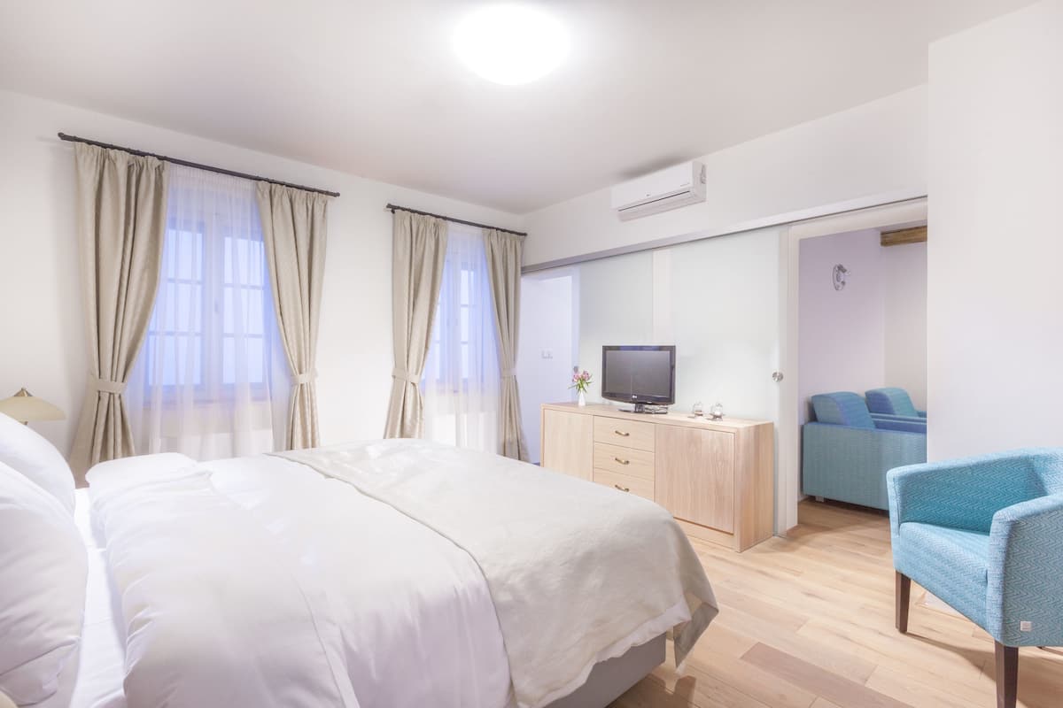 Habitación de hotel con una cama grande, un escritorio con televisión, una silla azul y una puerta corrediza que da a otra habitación.