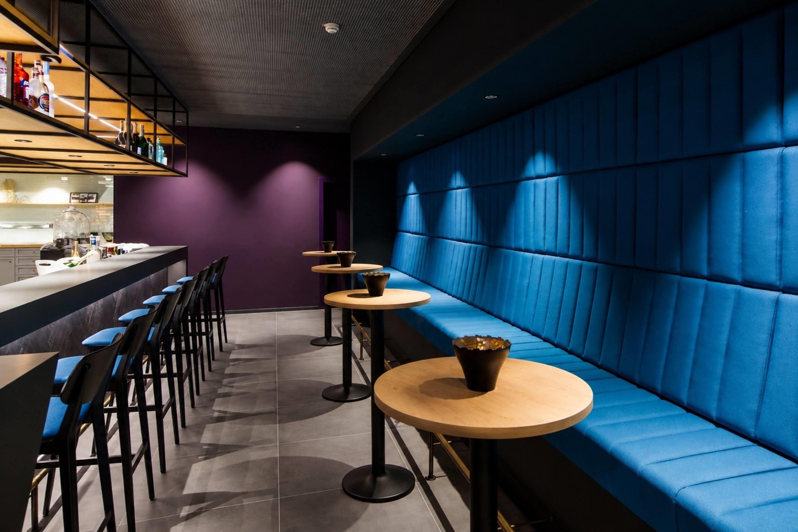 A modern bar area with blue upholstered seating, wooden tables, and black chairs.