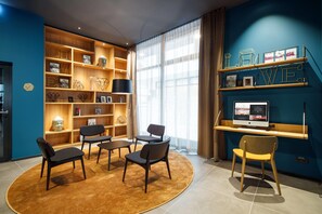 Una sala de estar moderna con una pared azul de acento, un ventanal con cortinas translúcidas, una mesa de centro redonda y una estantería con objetos decorativos.