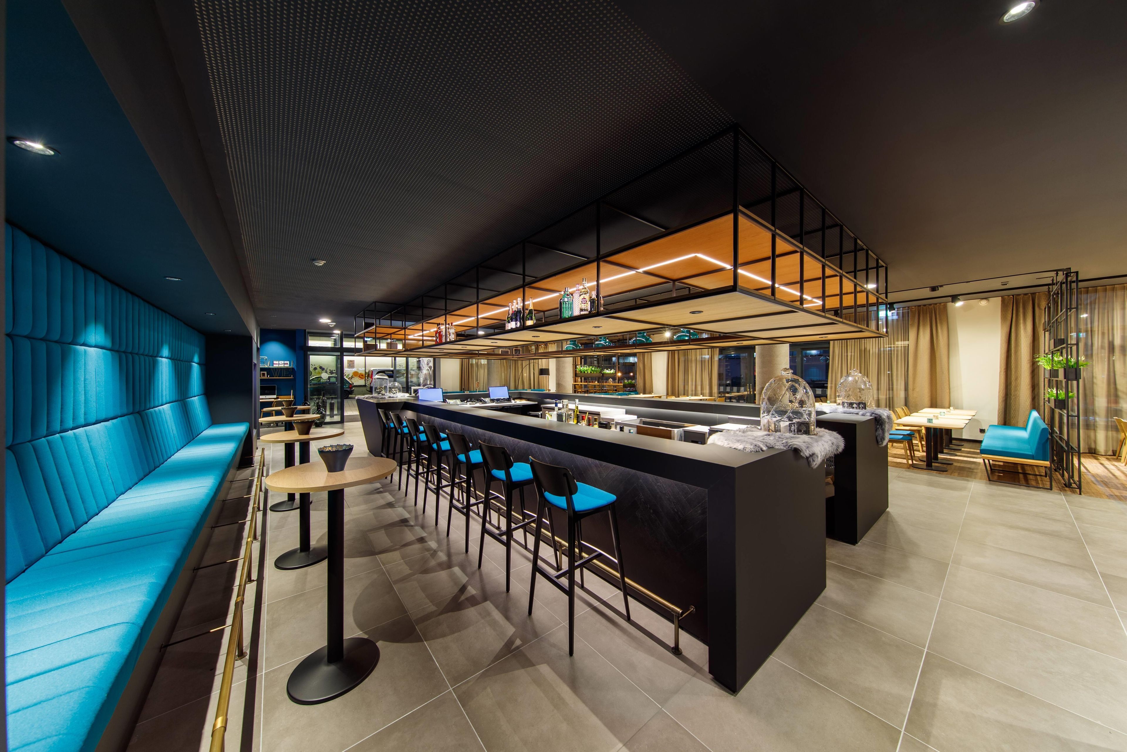 Un'area bar moderna con soffitto alto, sedute blu e un bancone con sgabelli.