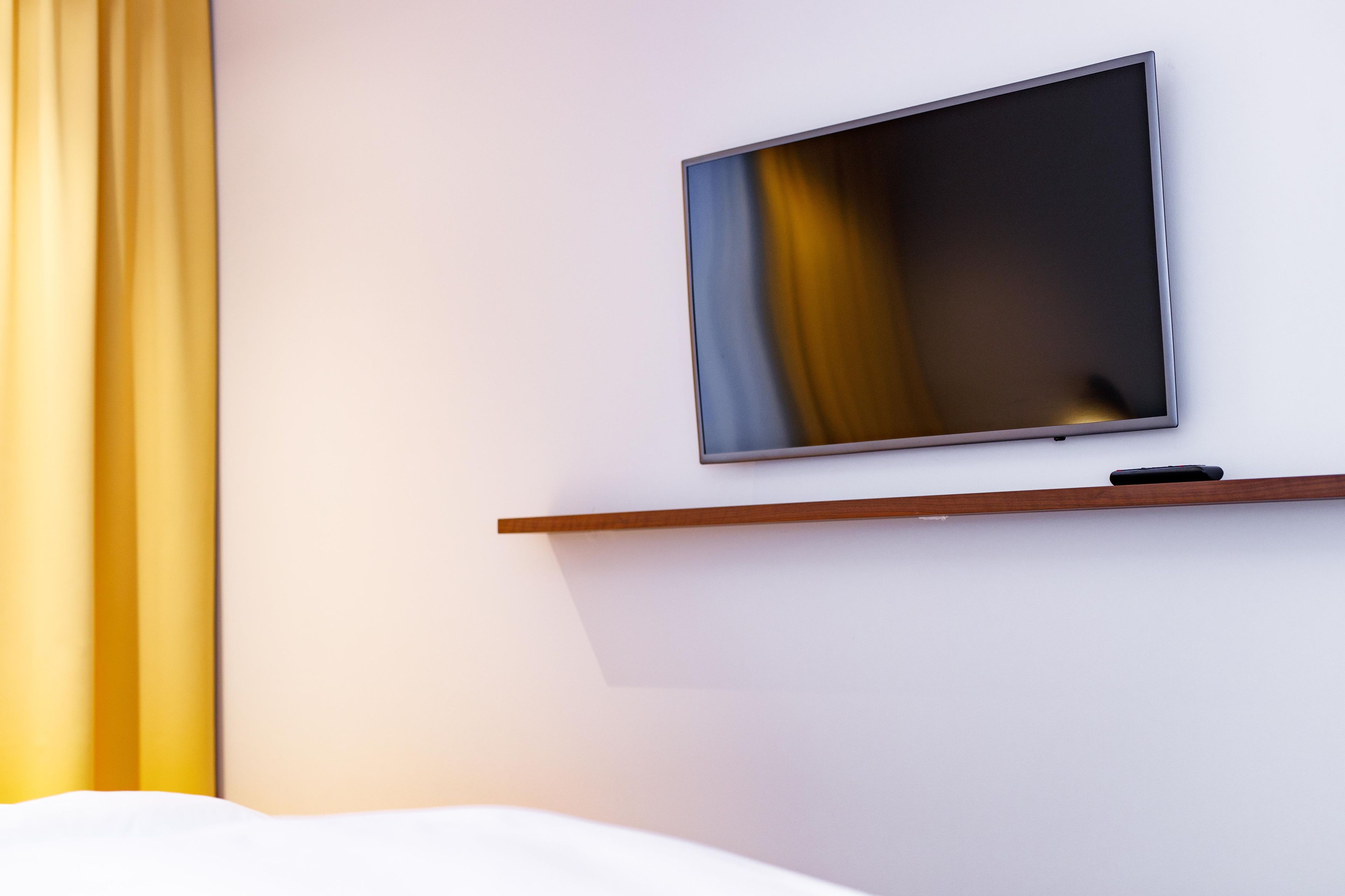 A television mounted on a wall with a wooden shelf below it.