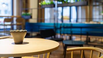 Interior de un restaurante con una mesa redonda, sillas, un área con asientos tipo banqueta azul y plantas colgantes.