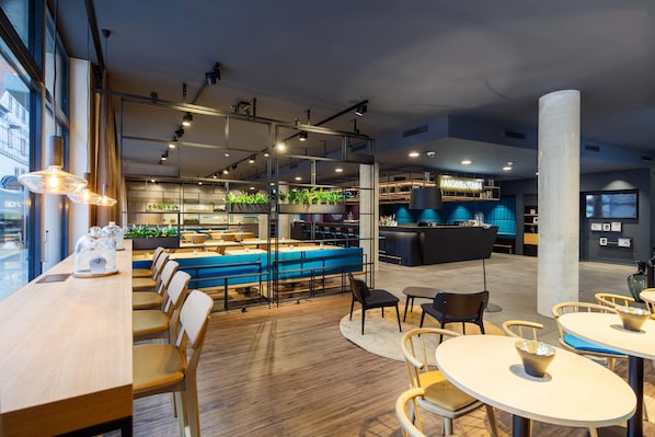A modern restaurant with a bar area, seating arrangements, and a view of the cityscape through large windows. - elaya hotel goeppingen, Trademark Collection by Wyndham (Goeppingen)