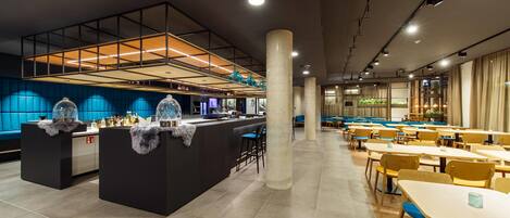 A modern restaurant with a central bar area, seating arrangements, and a high ceiling with lighting fixtures.
