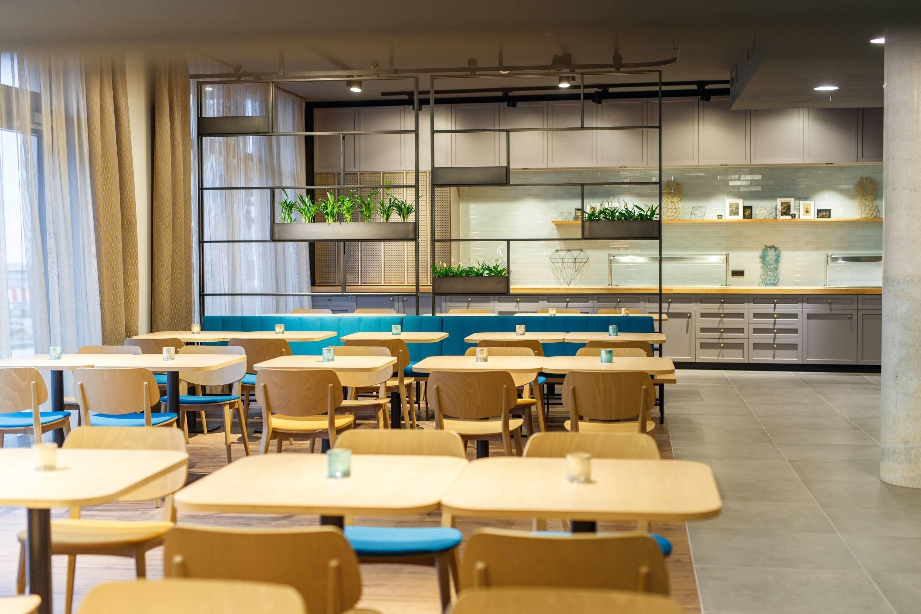 A modern restaurant interior with multiple seating areas, including tables and booths, and a counter with a display of plants and decorative items.
