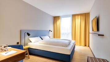 A hotel room with a bed, a desk, a chair, a TV, and a window with curtains.