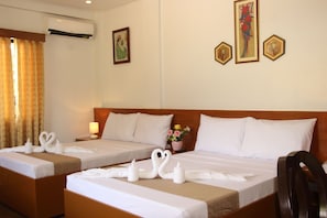 A hotel room with two beds, each with white linens and decorative swan-shaped towels. There is a wooden headboard, a nightstand with a lamp, and a wall-mounted air conditioner. - Casa Belina Tourist Inn (Puerto Princesa)