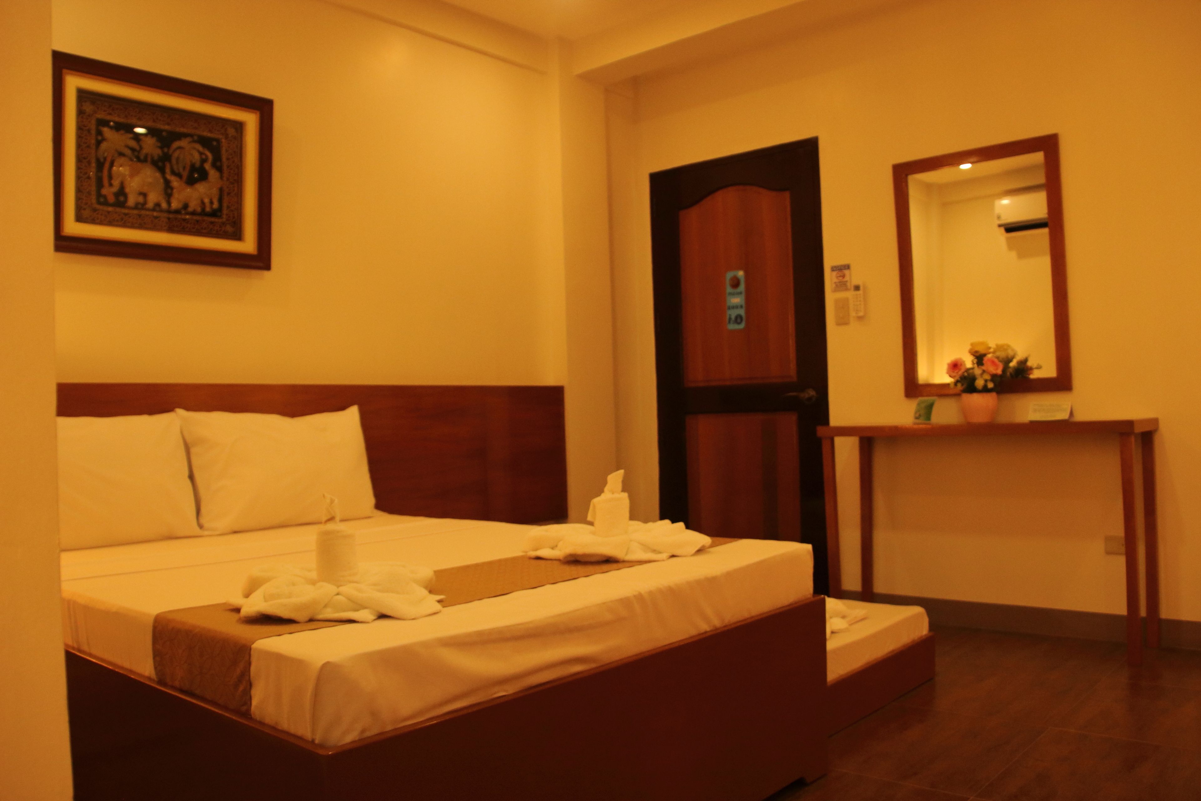 A hotel room with a bed, a wooden headboard, a bedside table with a mirror, and a framed picture on the wall.