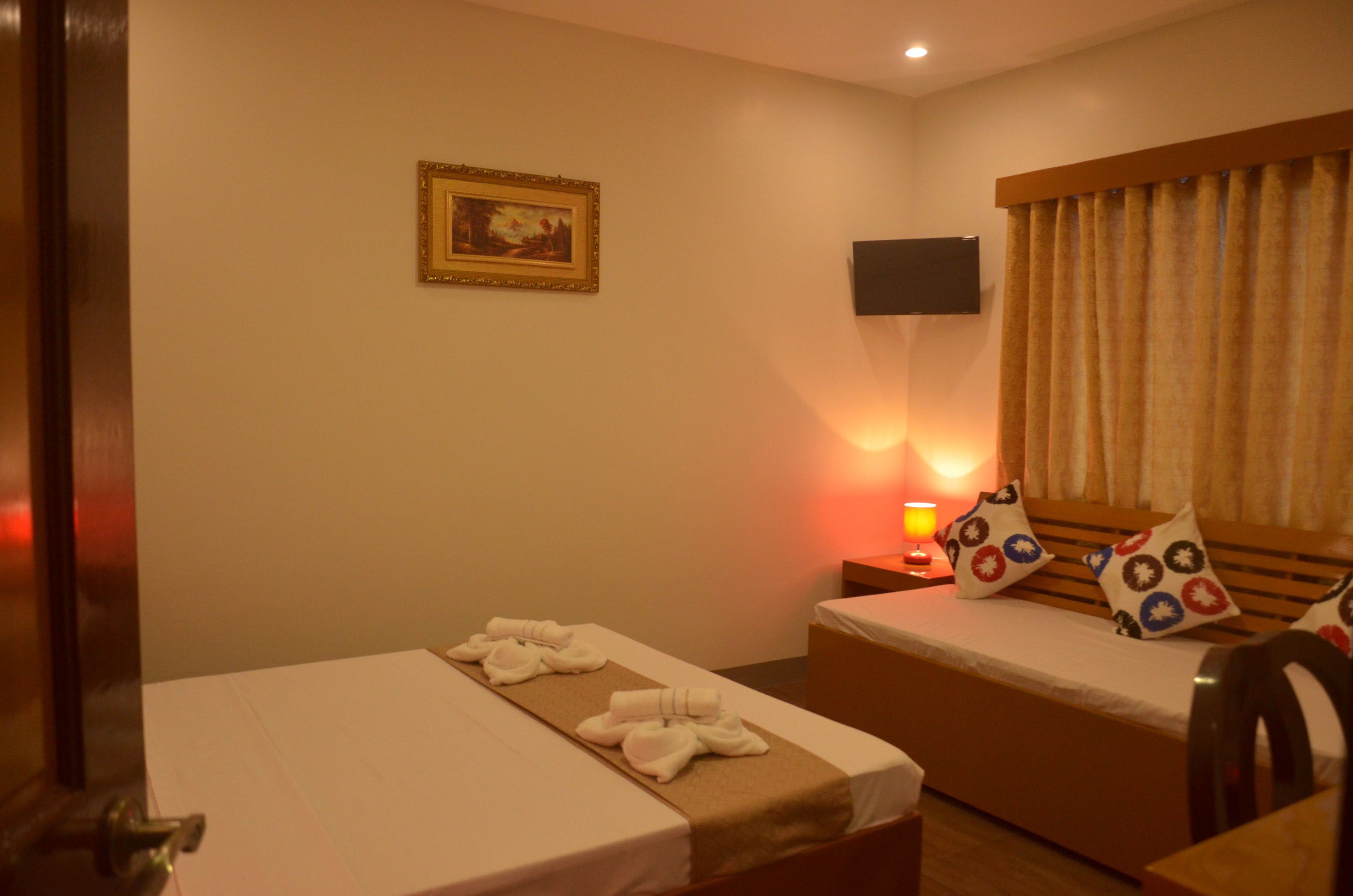 A hotel room with a bed, a bedside table with a lamp, a TV mounted on the wall, and a window with curtains.