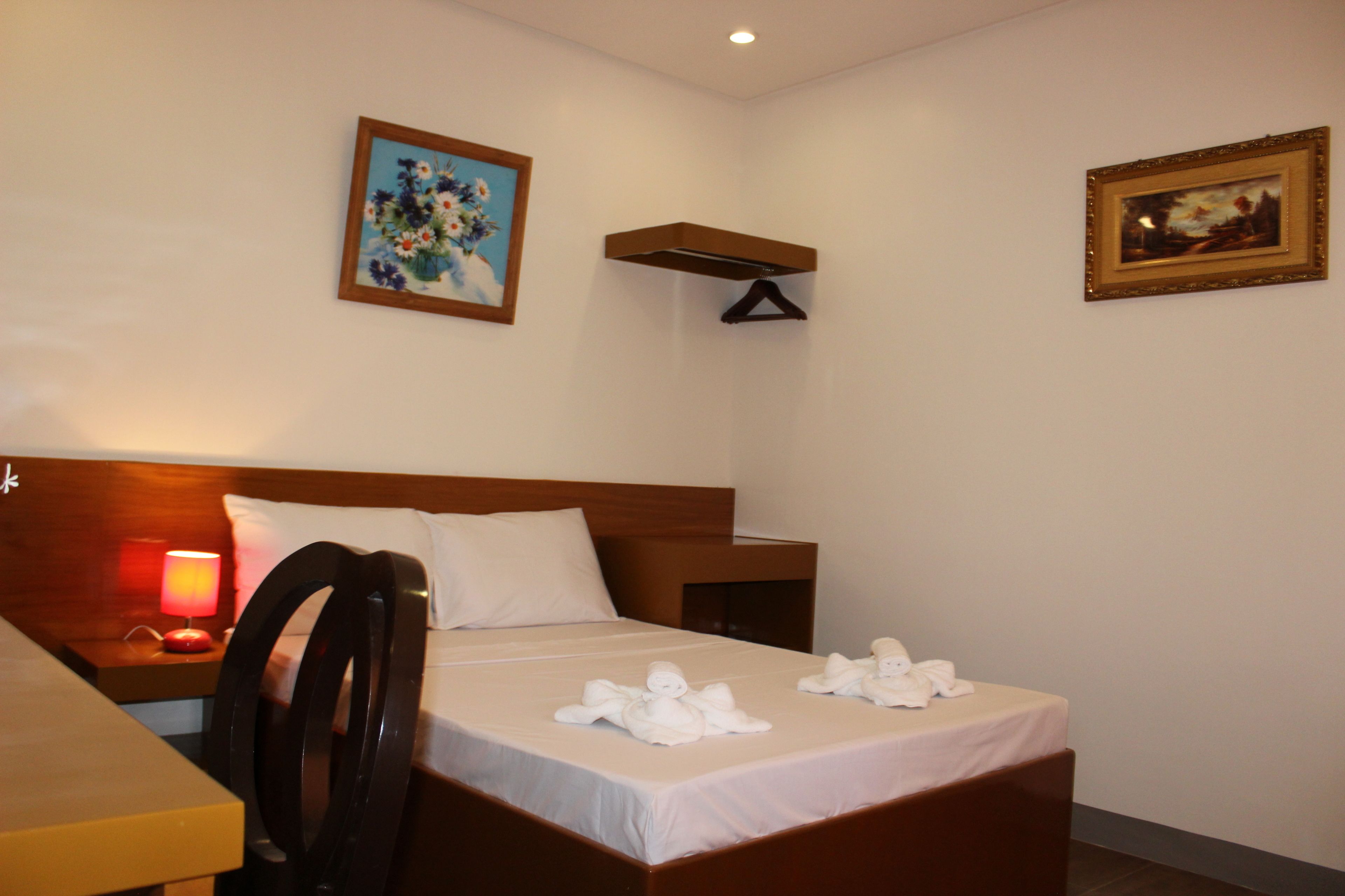 Ein Hotelzimmer mit Bett, Nachttisch mit Lampe, zwei Bildern an der Wand und einem Holz-Kopfteil.