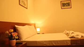 Ein Hotelzimmer mit einem Bett, einem Nachttisch mit Lampe, einer Blumenvase und zwei gerahmten Bildern an der Wand.