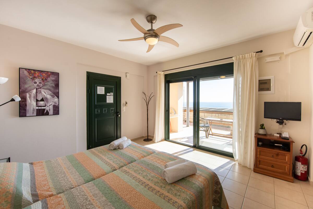 Une chambre d’hôtel avec un lit, un ventilateur de plafond, une télévision, un extincteur et une vue sur la plage.