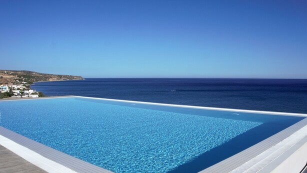Una piscina infinita de color azul cristalino con vista al mar y a la costa distante.