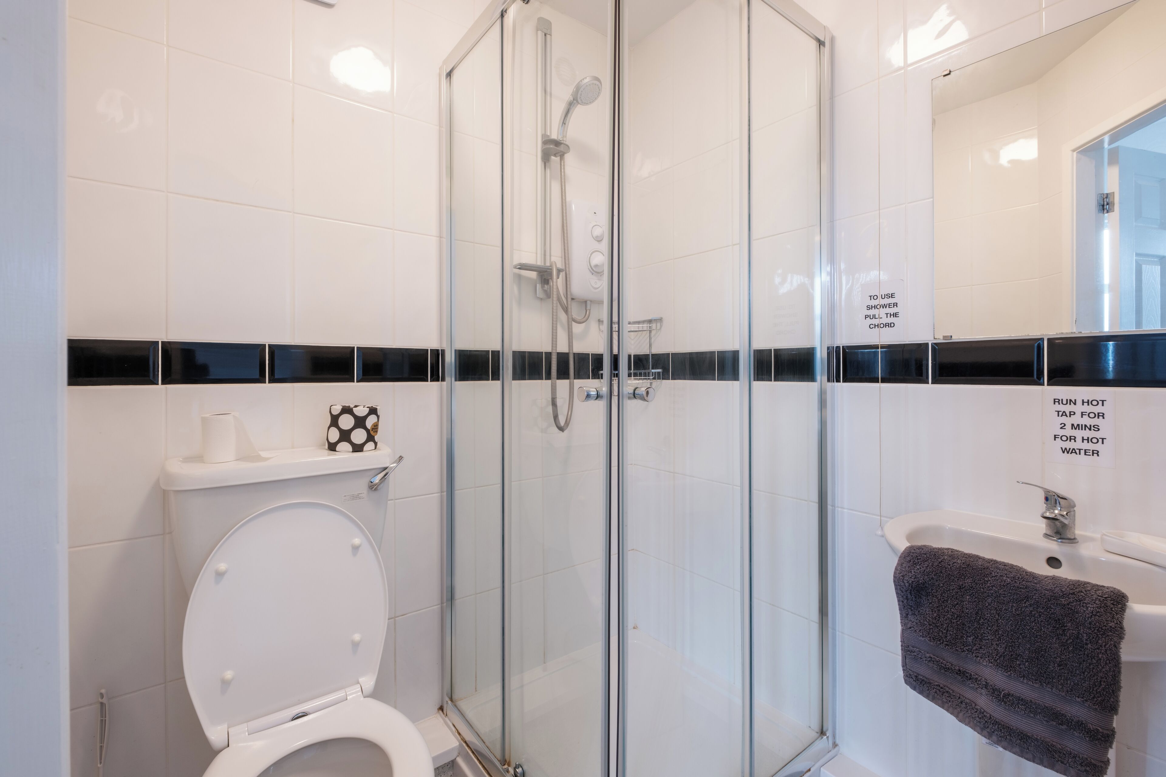 Un baño moderno con ducha envuelta en vidrio, inodoro blanco y lavamanos con una toalla colgada en la pared.