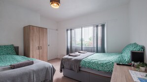 A bedroom with two beds, a wardrobe, a desk with a lamp, and a window with curtains. - OYO The Pickering Park (Hull)