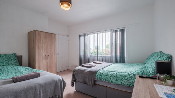 Un dormitorio con dos camas, un armario, un escritorio con lámpara y una ventana con cortinas.