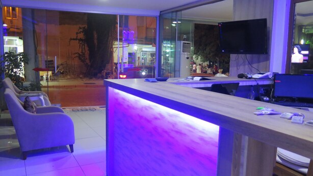 A reception area with a counter, seating, and a TV screen. - Lidya City Hotel (Fethiye)