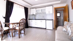 A modern kitchen with white cabinets, a dining table with chairs, and a sofa in a bright living area. - Lidya City Hotel (Fethiye)