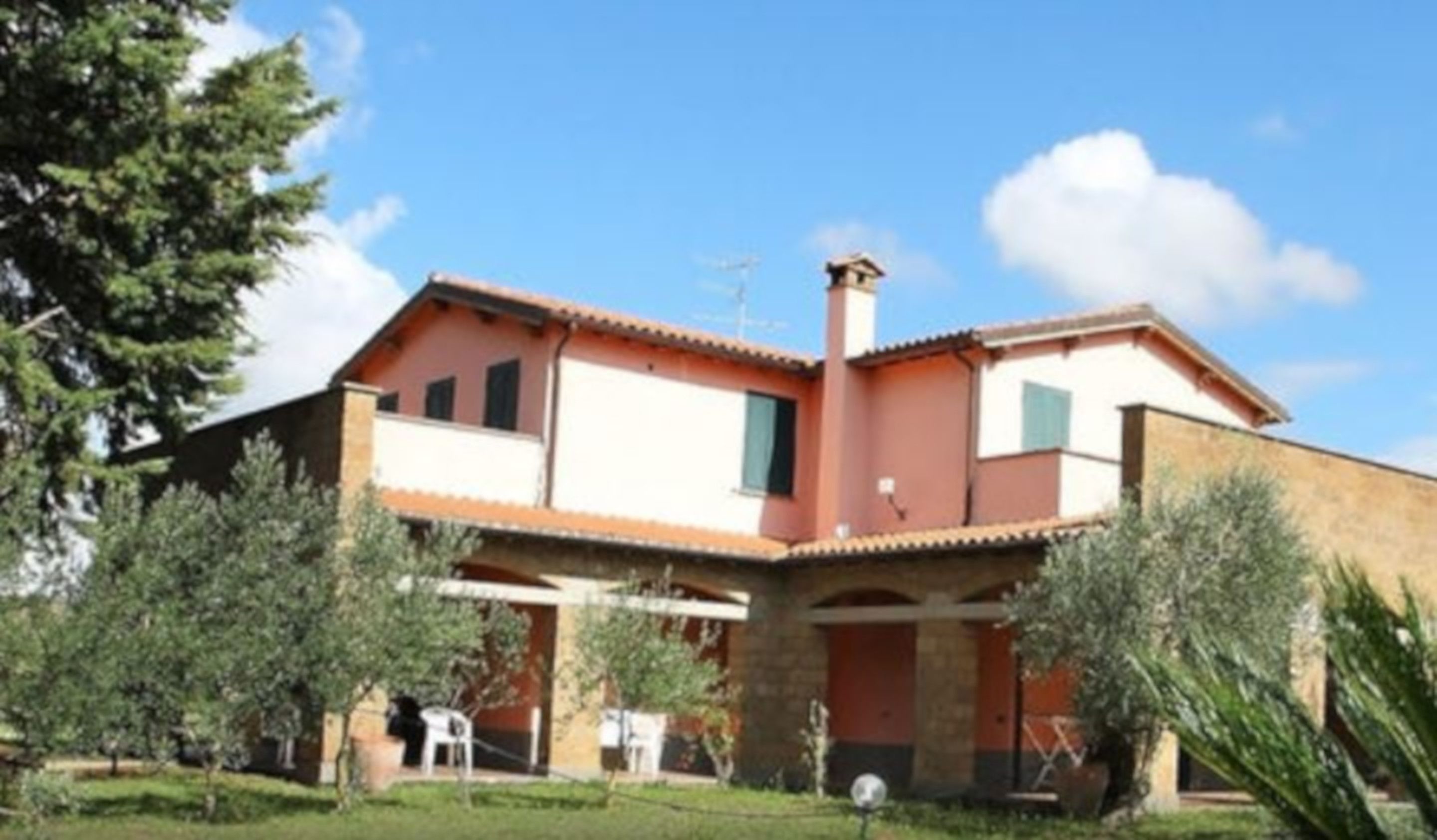 Une maison à deux étages, avec un toit en tuiles, une cheminée et un jardin agrémenté d’arbres et d’une pelouse.