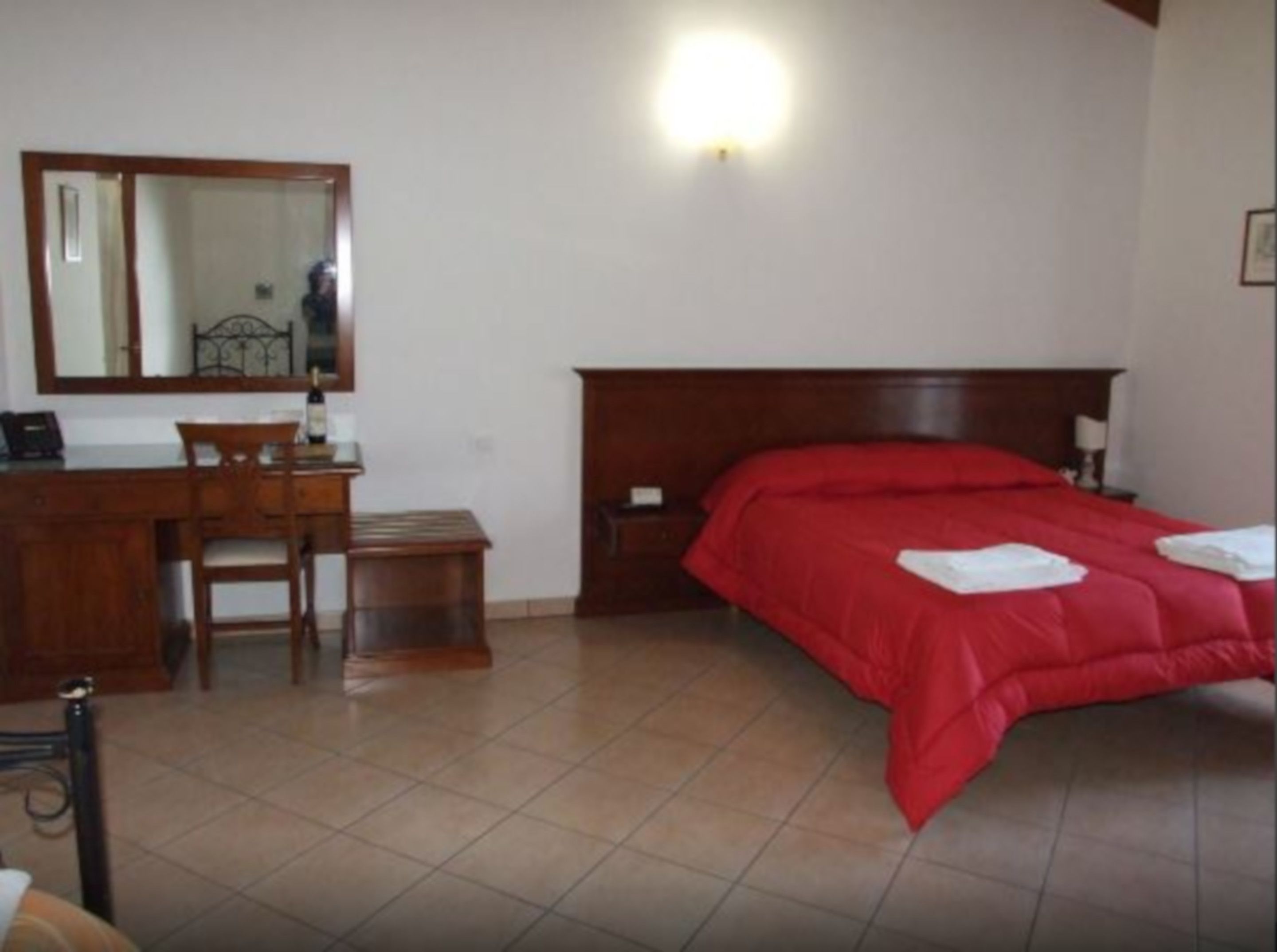 Quarto com escrivaninha de madeira, cadeira e cama com roupa de cama vermelha.