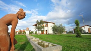 Une sculpture représentant une figure dans un jardin, avec un bâtiment en arrière-plan.