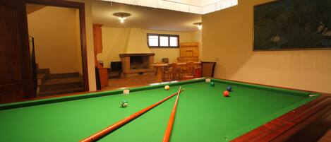 A pool table with pool cues and balls, a wooden cabinet, and a painting on the wall.