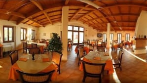 Un vaste espace dédié à la salle à manger, doté de hauts plafonds et de poutres en bois, et comprenant plusieurs tables et chaises.