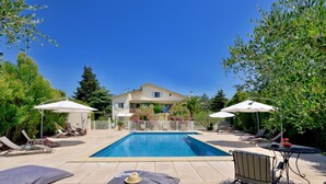 Piscina con lettini e ombrelloni, circondata da una recinzione e alberi.