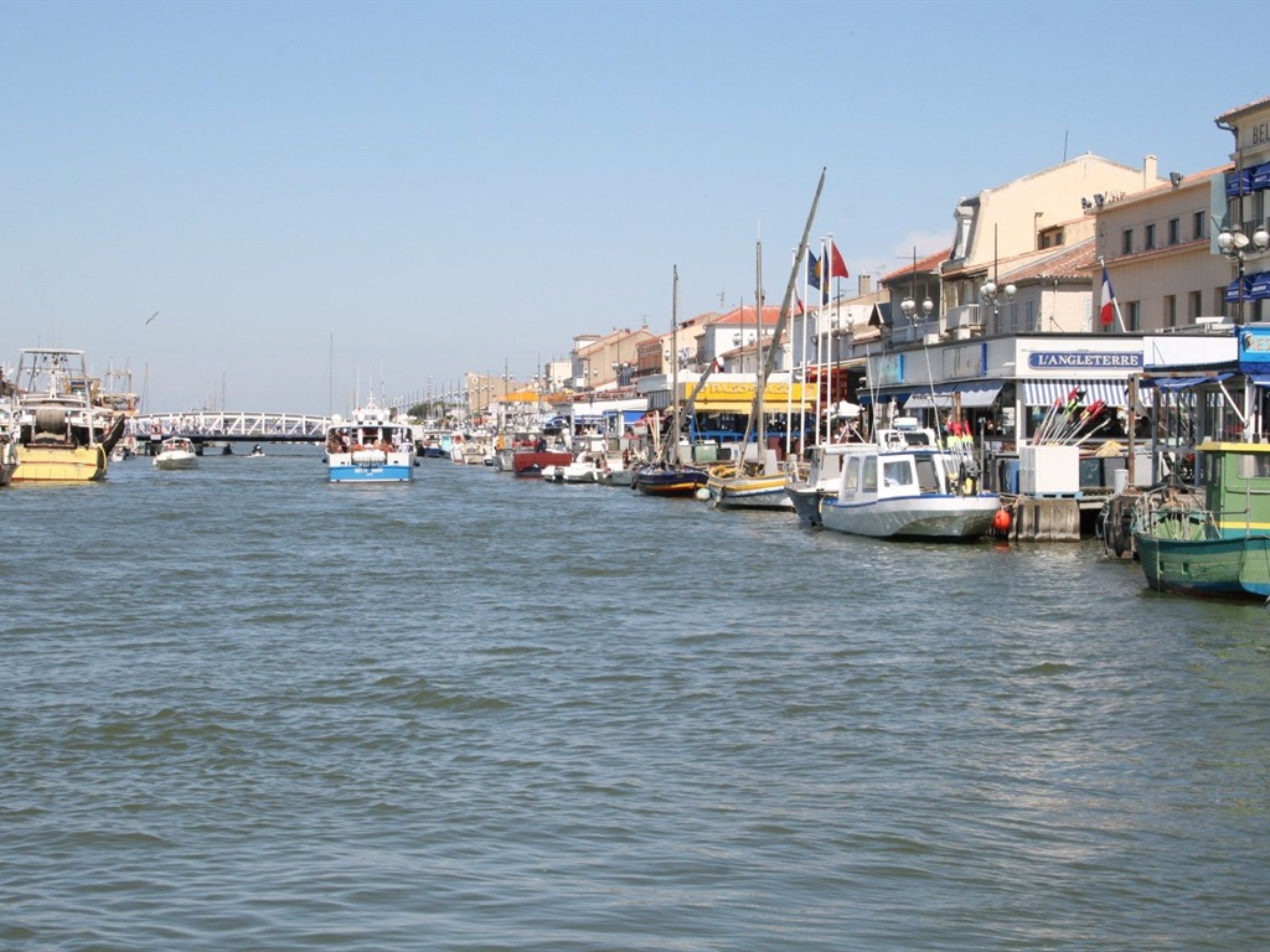A marina with various boats docked along the waterfront, surrounded by buildings with commercial establishments.