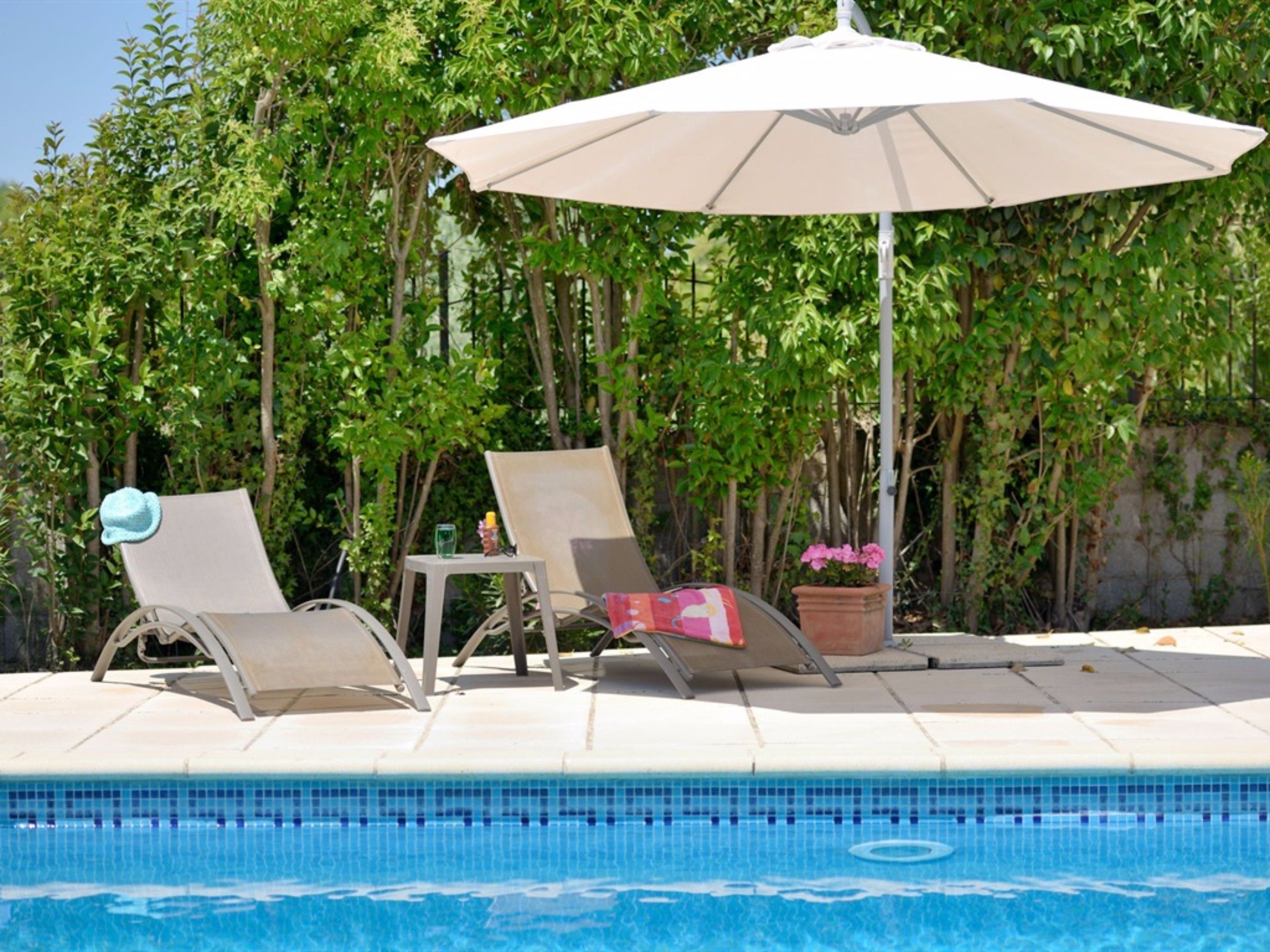 A poolside area with two lounge chairs, a table, and a large umbrella.
