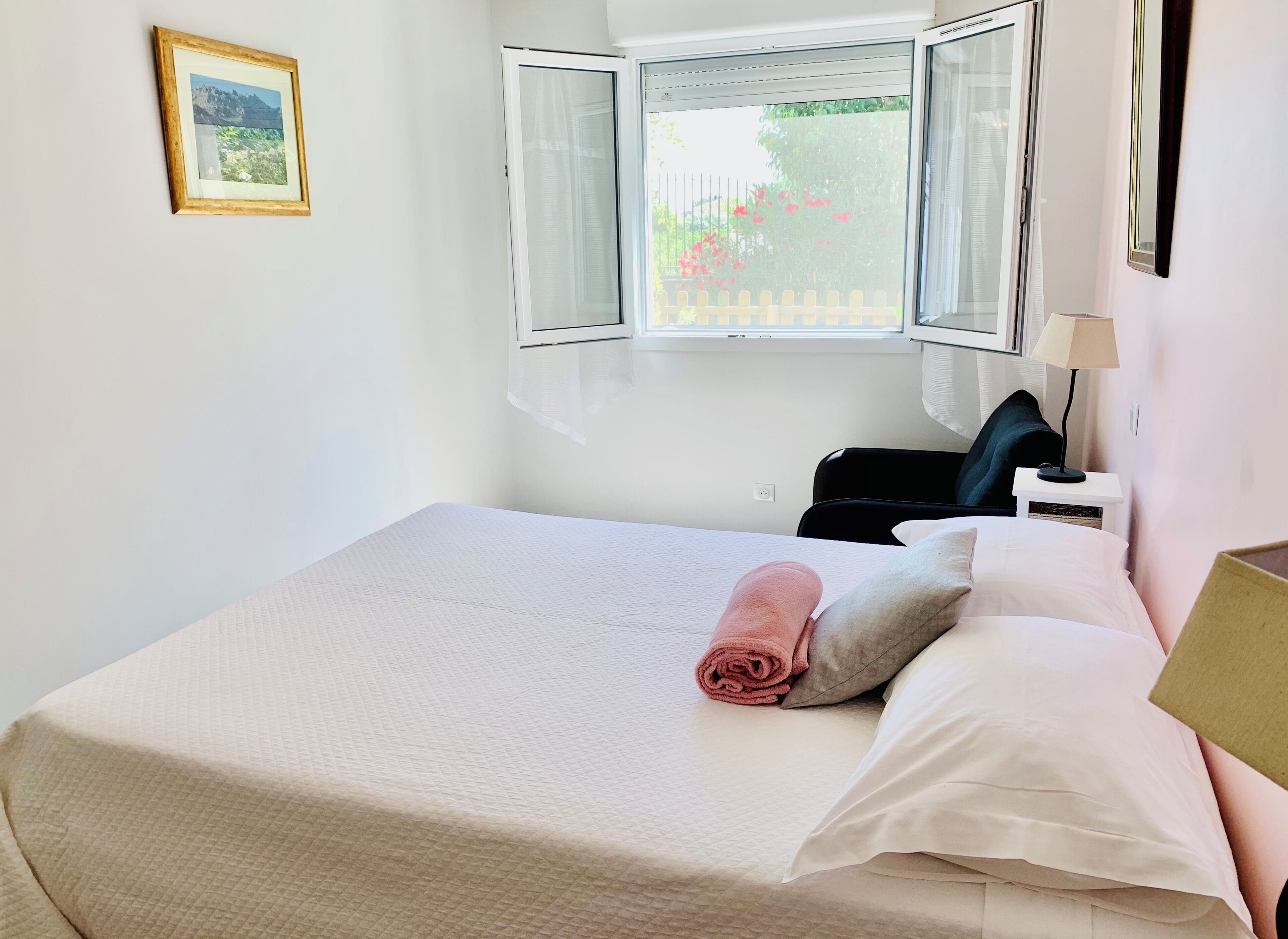 A neatly made bed with a rolled towel, a bedside lamp, and a window with curtains.