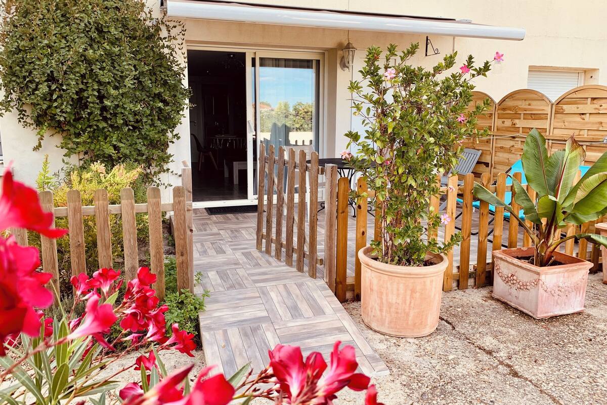 A wooden gate leading to a covered entrance, a potted plant, and a patio area with a wooden fence.