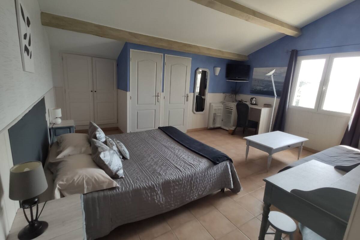 A bedroom with a bed, bedside tables, a desk, and a chair. There is a wardrobe, a mirror, and a window.